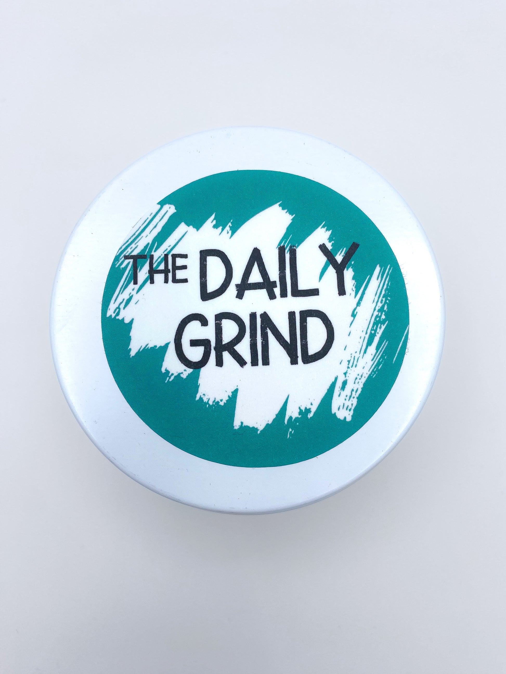 White candle lid with "The Daily Grind" label